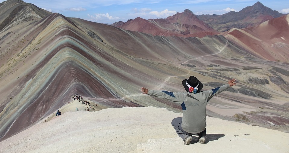Vinicunca in Peru mit Person mit ausgebreiteten Armen im Vordergrund