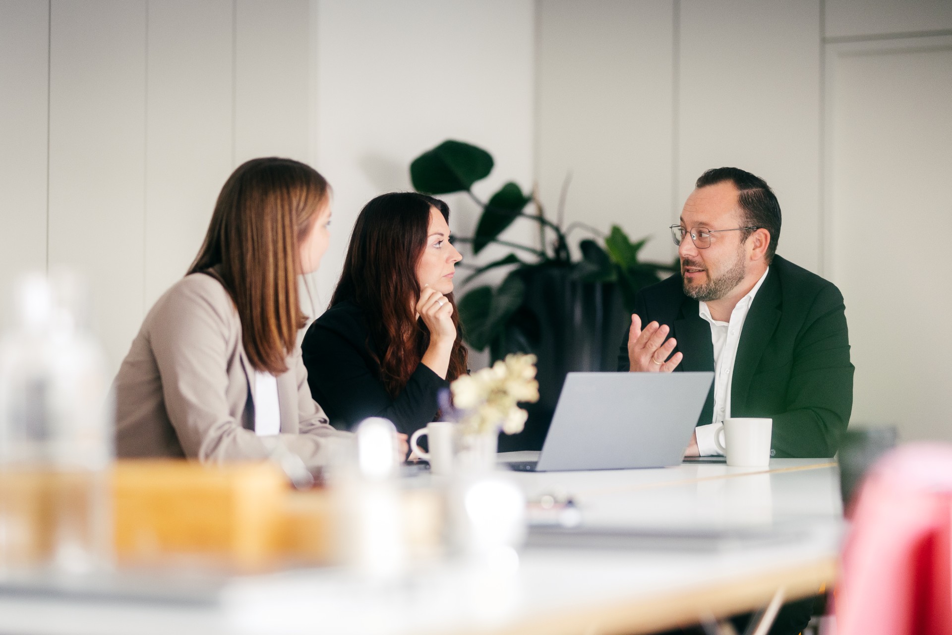 Three business people are sitting at a table with a laptop, deeply engaged in a conversation.
