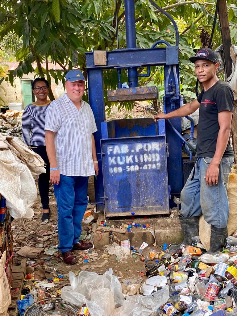 zwei Männer mit einer Presse zum Pressen von Plastikflaschen im Hintergrund