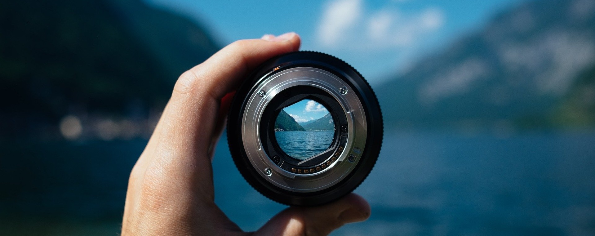 Kameralinse wird vor einen See mit Bergen gehalten.