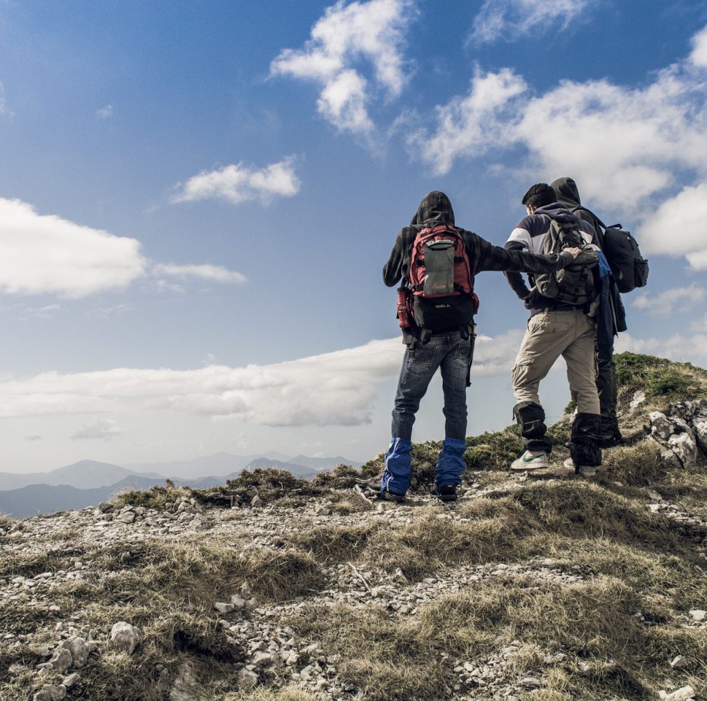 Drei Bergsteiger stehen auf einem Gipfel und schauen in die Ferne.