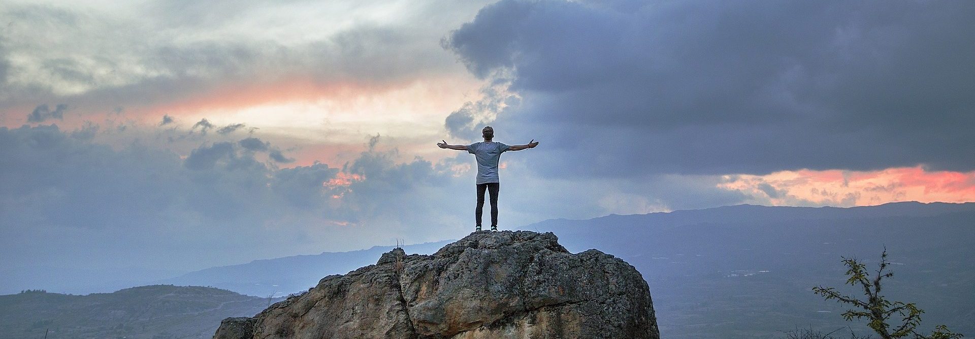 Ein Mann steht mit ausgebreiteten Armen in der Abenddämmerung auf einem Felsen.