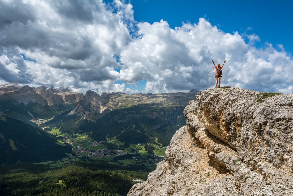 Eine Wanderin steht auf einem Felsen, streckt die Arme nach oben und schaut in das Tal vor ihr.