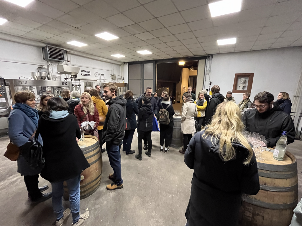 Participants standing around wine barrels and participating in a wine tasting.